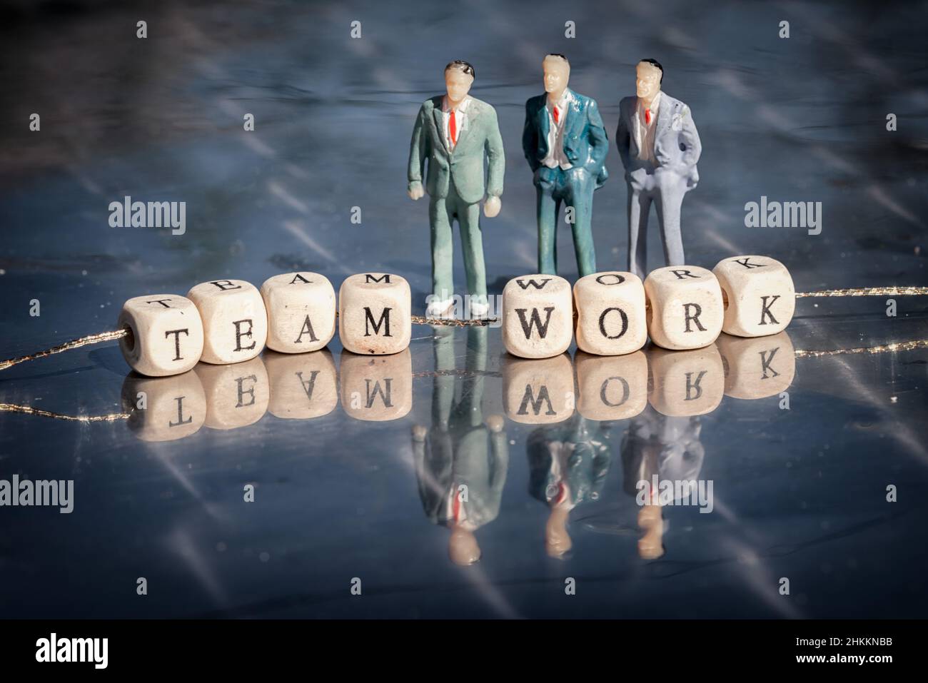 Miniatur-Modell von Geschäftsleuten und Holzwürfel mit Teamwork-Beschriftung auf einem Faden auf reflektierenden Tisch aufgereiht. Das Team arbeitet Geschäftskonzept. Stockfoto
