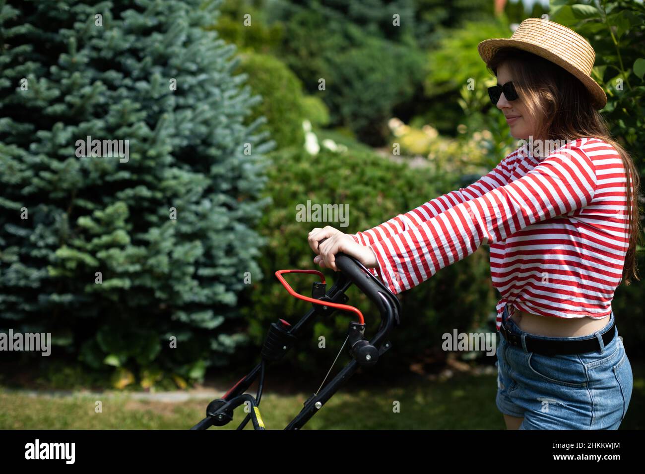 Ein Mädchen hält den Griff eines Gartenmähers in den Händen. Stockfoto