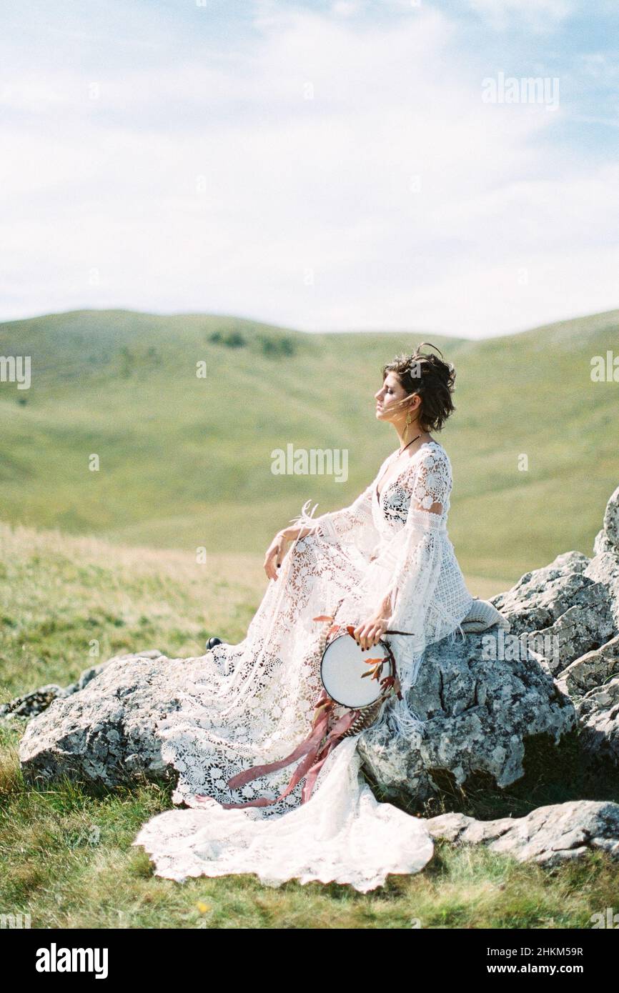 Mädchen in einem weißen Kleid mit einem Tamburin in der Hand sitzt auf Steinen Stockfoto