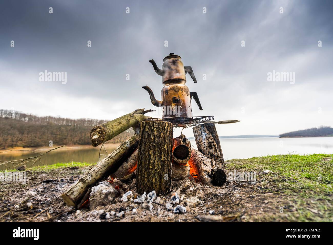 Türkische traditionelle Teekannen kochten am Lagerfeuer, ein glatter See im Hintergrund. Stockfoto