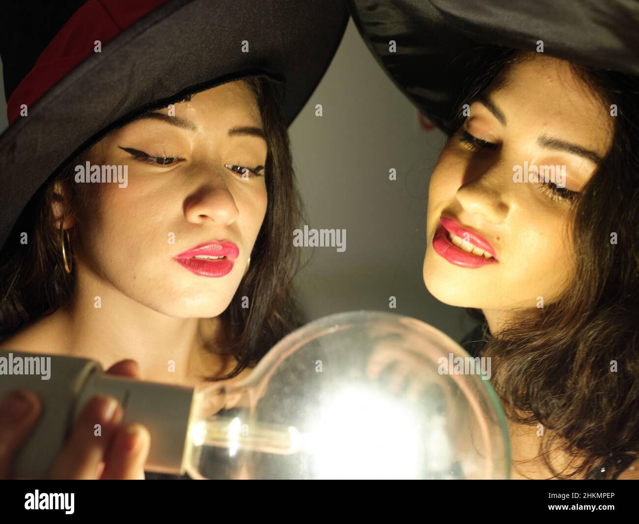 Zwei Latina-Freunde, die an halloween als Hexen gekleidet waren, mit einer Glühbirne in ihrer Nähe und schauten sich diese an. Stockfoto