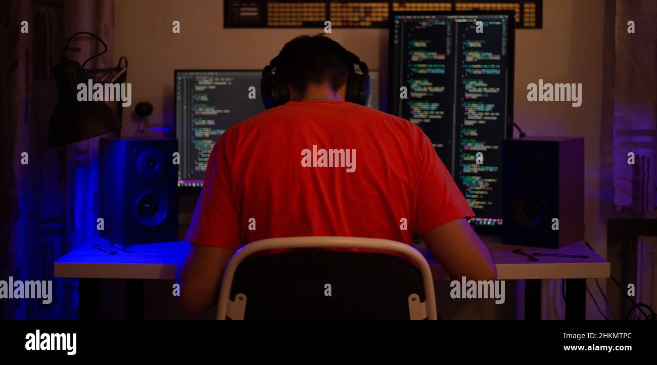 Ein Mann sitzt nachts in einem Raum an einem Tisch mit blauer Beleuchtung und Programmen an einem Computer Stockfoto