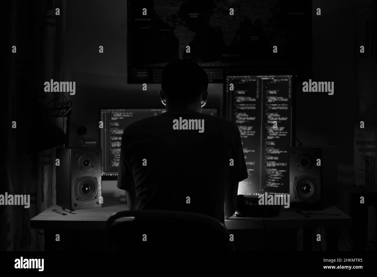 Ein Mann sitzt nachts in einem Raum an einem Tisch mit blauer Beleuchtung und Programmen an einem Computer Stockfoto
