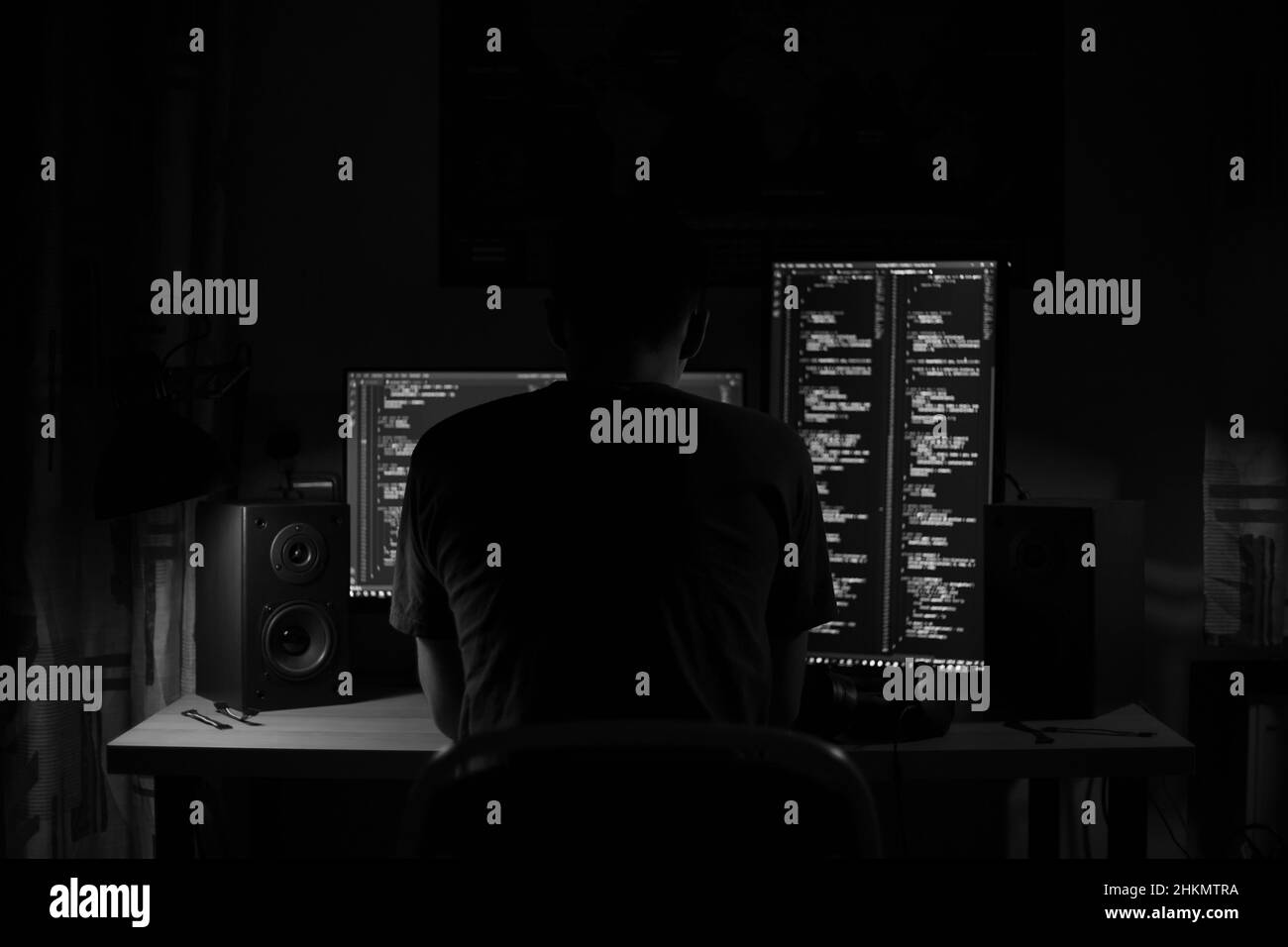 Ein Mann sitzt nachts in einem Raum an einem Tisch mit blauer Beleuchtung und Programmen an einem Computer Stockfoto