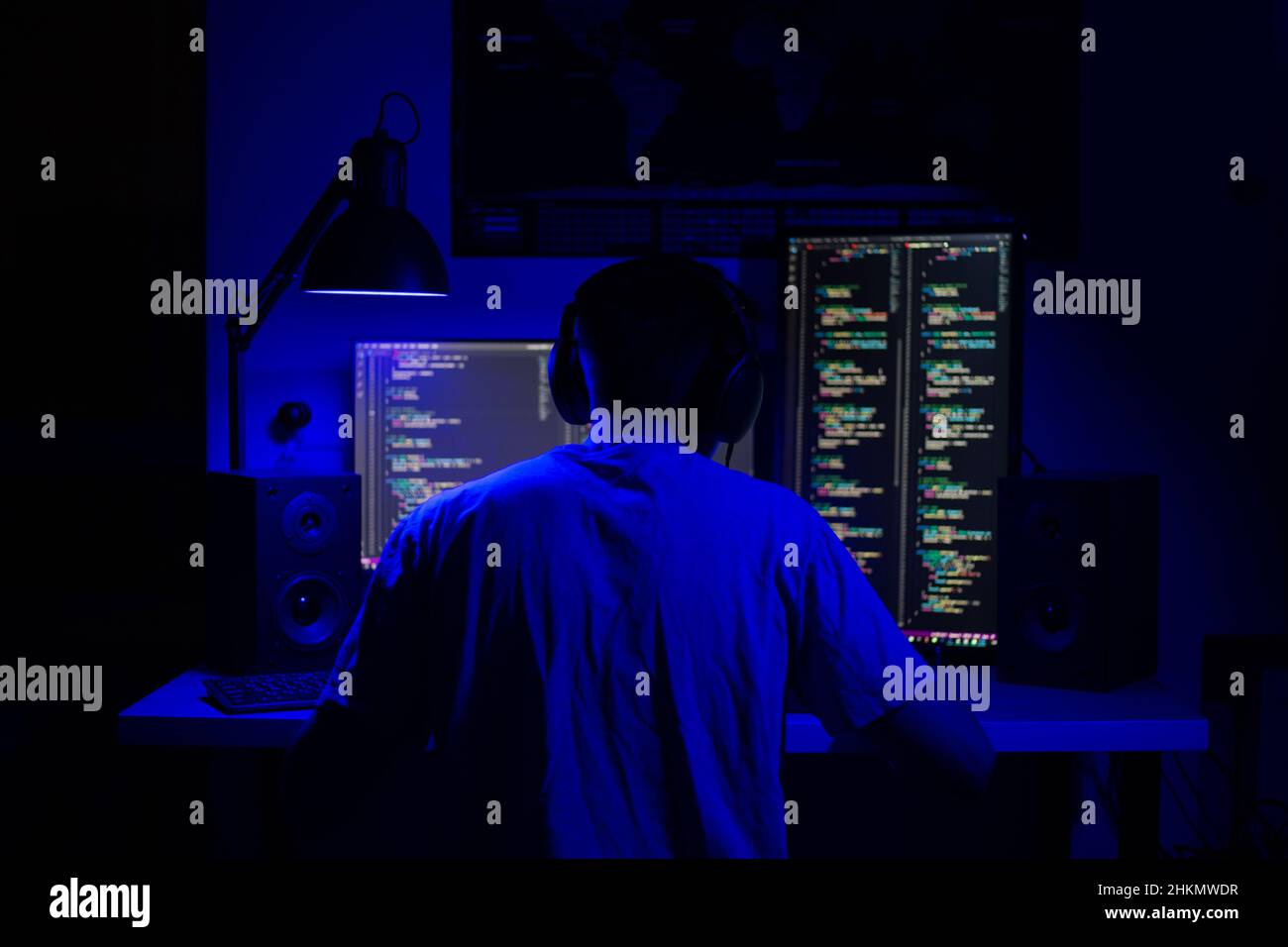 Ein Mann sitzt nachts in einem Raum an einem Tisch mit blauer Beleuchtung und Programmen an einem Computer Stockfoto