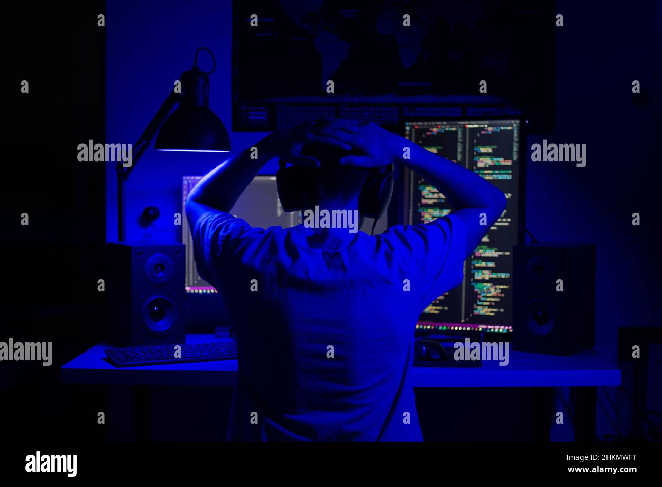 Ein enttäuschter Mann sitzt nachts in einem Raum an einem Tisch mit blauer Beleuchtung und Programmen an einem Computer Stockfoto
