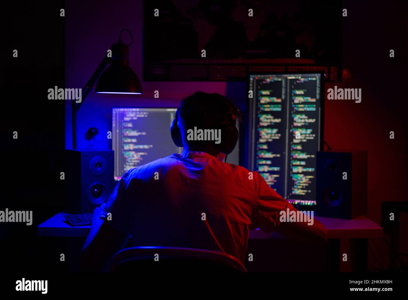 Ein Mann sitzt nachts in einem Raum an einem Tisch mit blauer Beleuchtung und Programmen an einem Computer Stockfoto