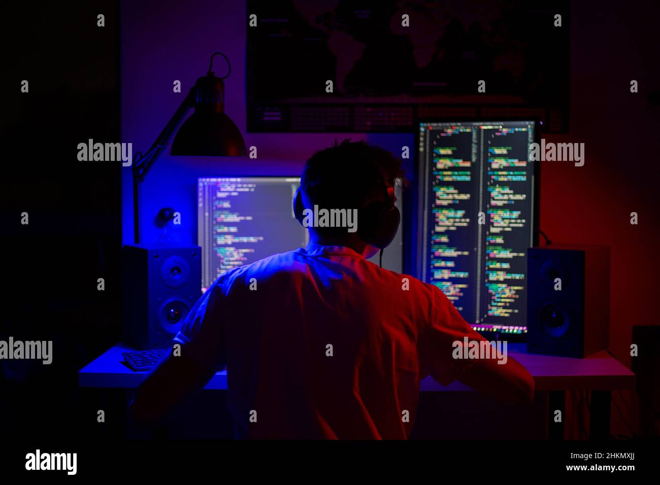 Ein Mann sitzt nachts in einem Raum an einem Tisch mit blauer Beleuchtung und Programmen an einem Computer Stockfoto