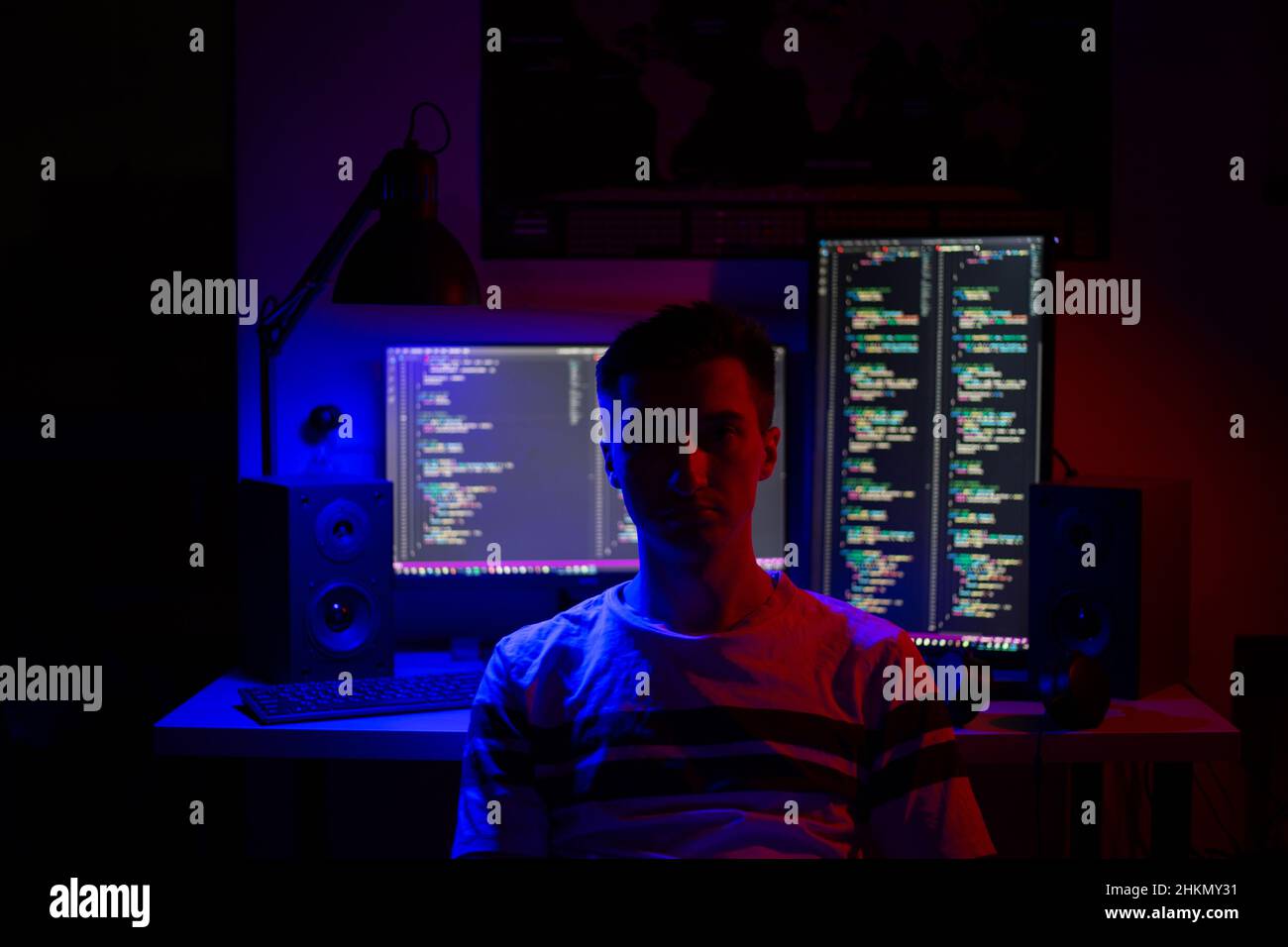 Ein Mann sitzt nachts in einem Raum an einem Tisch mit blauer Beleuchtung und Programmen an einem Computer Stockfoto