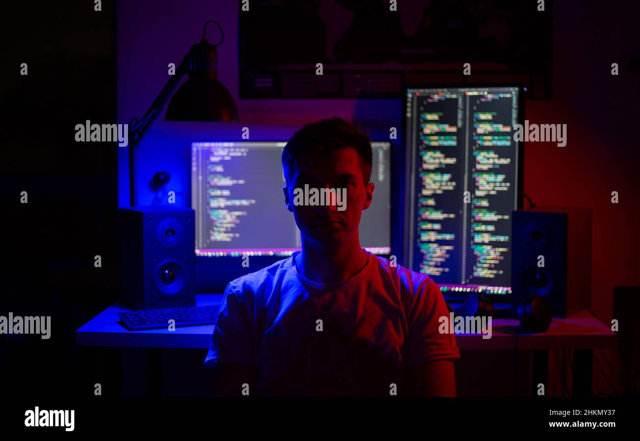 Ein Mann sitzt nachts in einem Raum an einem Tisch mit blauer Beleuchtung und Programmen an einem Computer Stockfoto