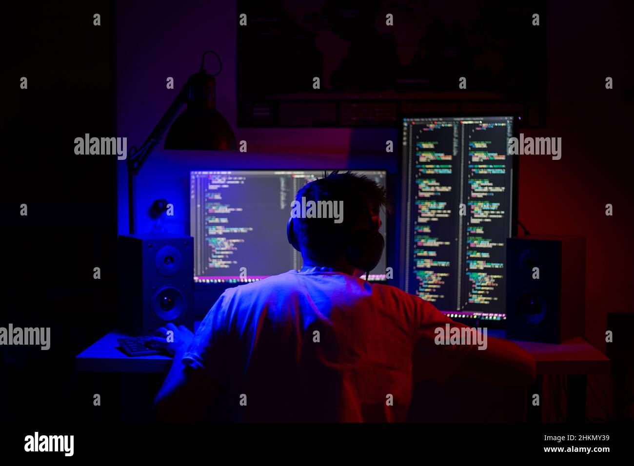 Ein Mann sitzt nachts in einem Raum an einem Tisch mit blauer Beleuchtung und Programmen an einem Computer Stockfoto