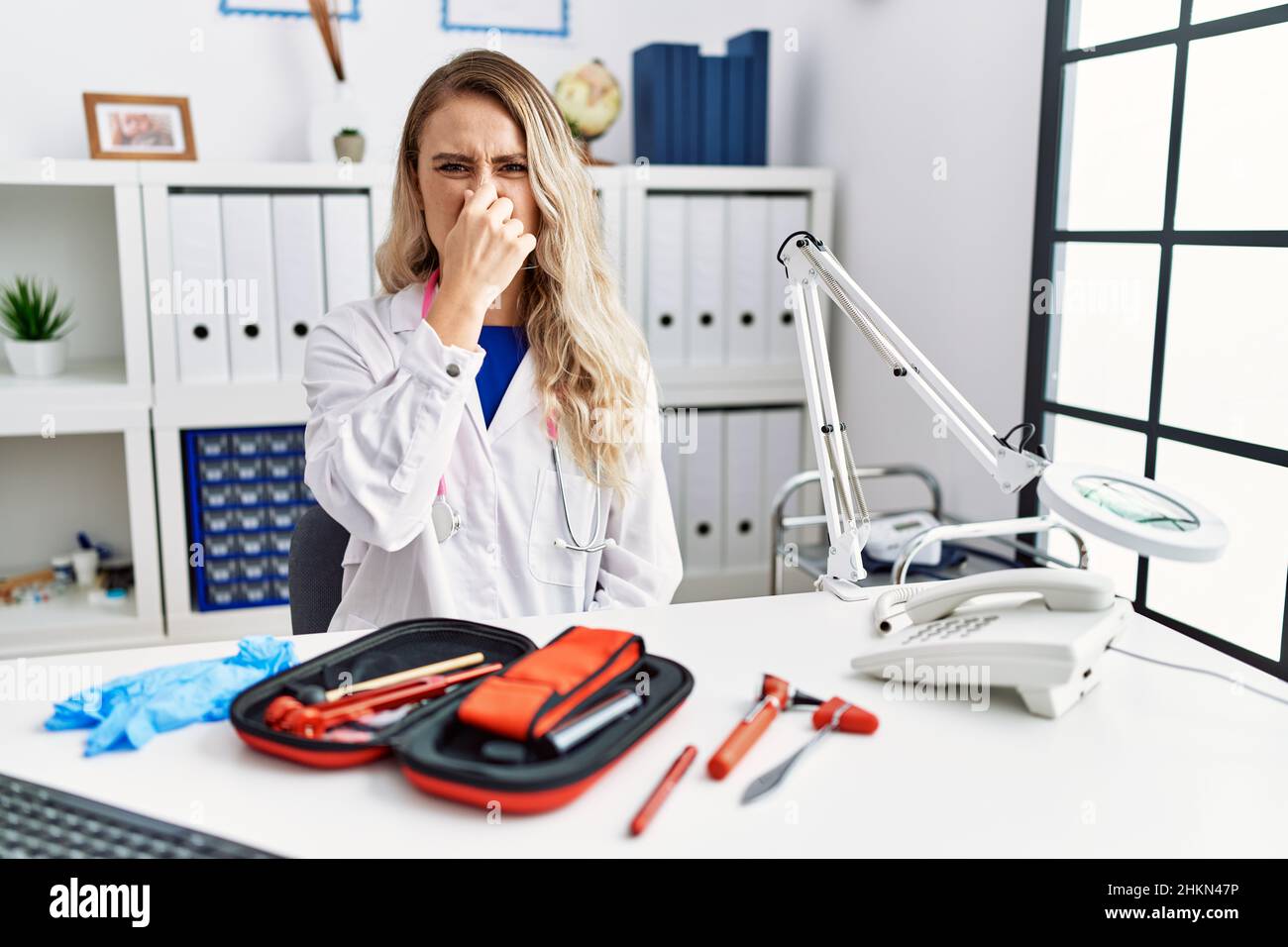 Junge schöne Ärztin mit Reflexhammer und medizinischen Instrumenten, die etwas stinkendes und