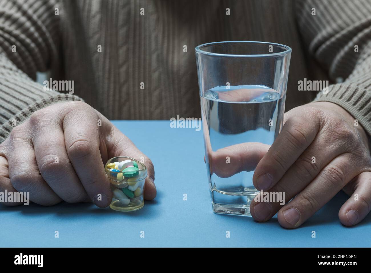 Ein Mann sitzt an einem Tisch und hält ein Glas Wasser und Pillen in den Händen. Stockfoto