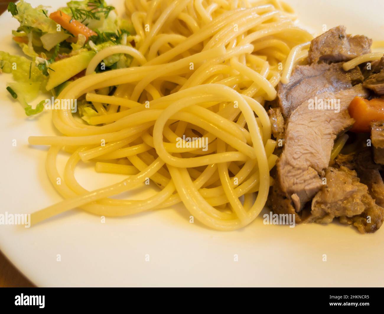 Blick aus der Nähe auf dem Teller mit Pasta, gebackenem Fleisch und Gemüsesalat Stockfoto