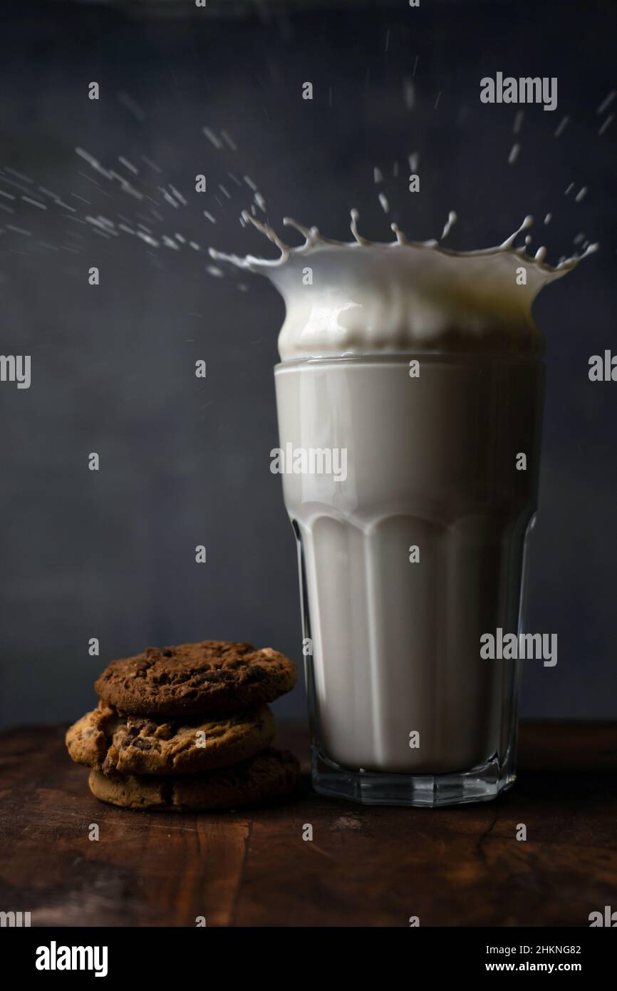 Milch in einem Glas spritzen und Schokoladenkekse auf einem Holztisch Stockfoto