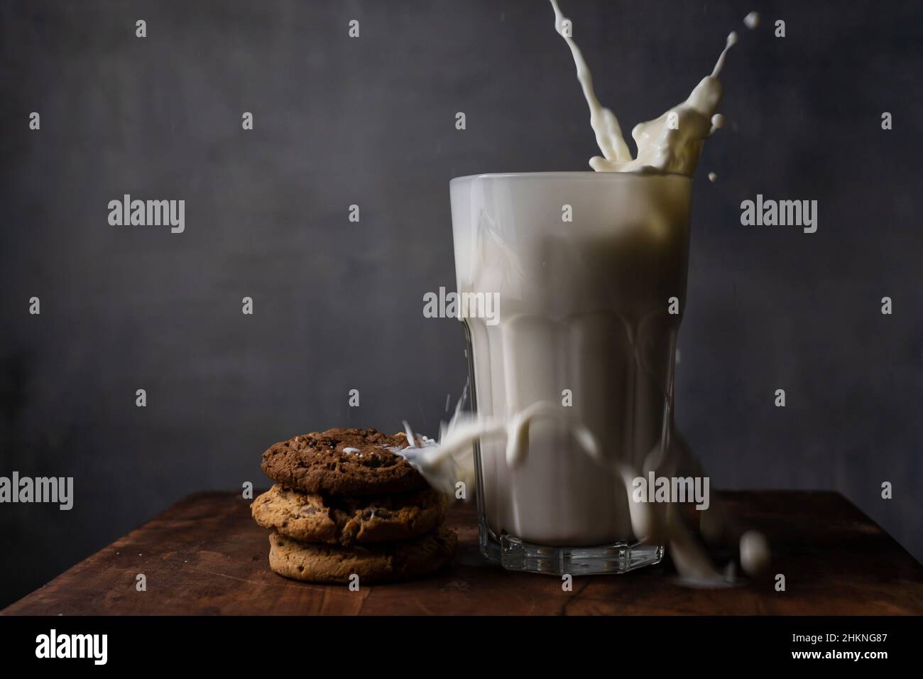 Milch in einem Glas spritzen und Schokoladenkekse auf einem Holztisch Stockfoto
