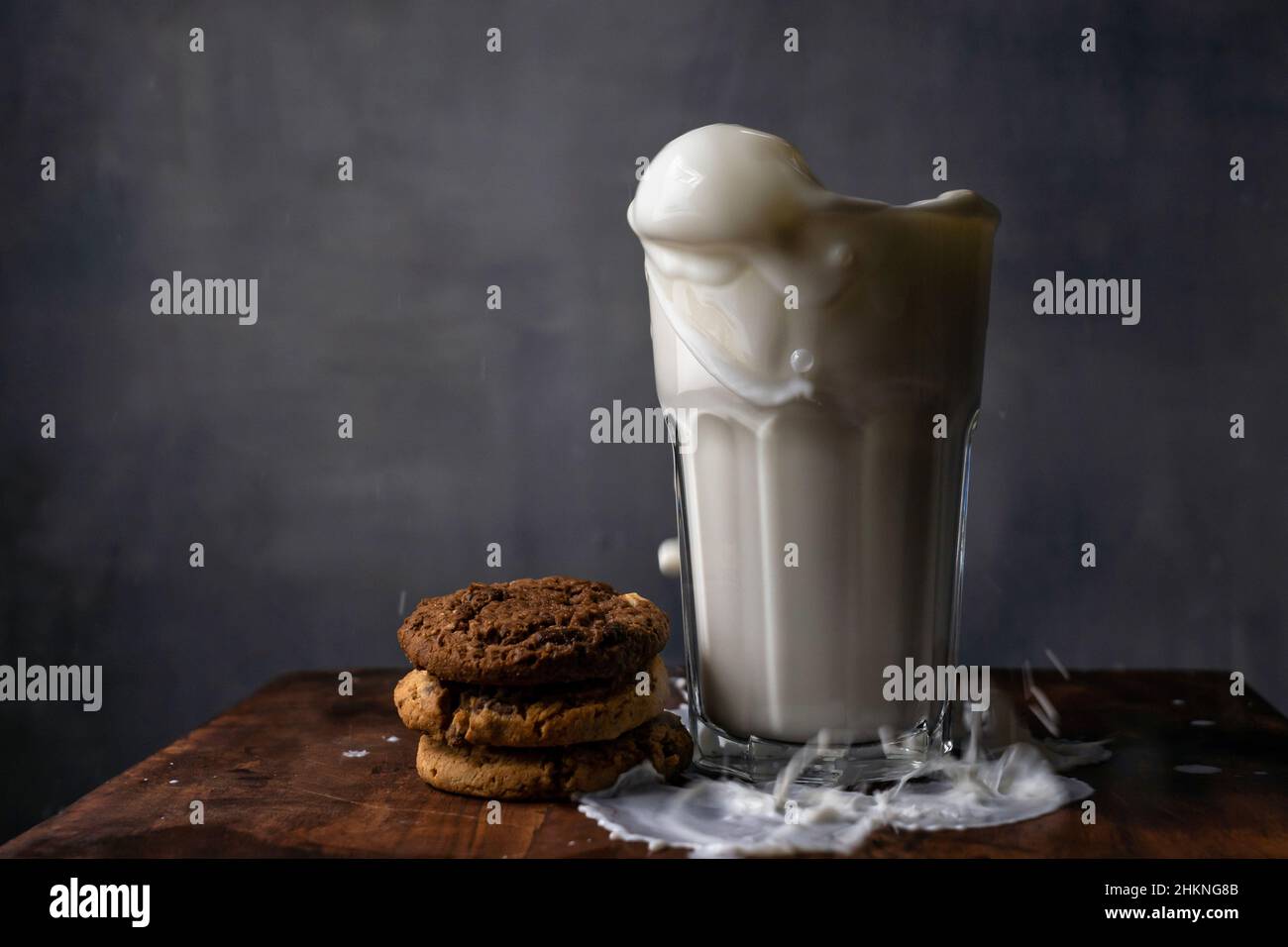 Milch in einem Glas spritzen und Schokoladenkekse auf einem Holztisch Stockfoto