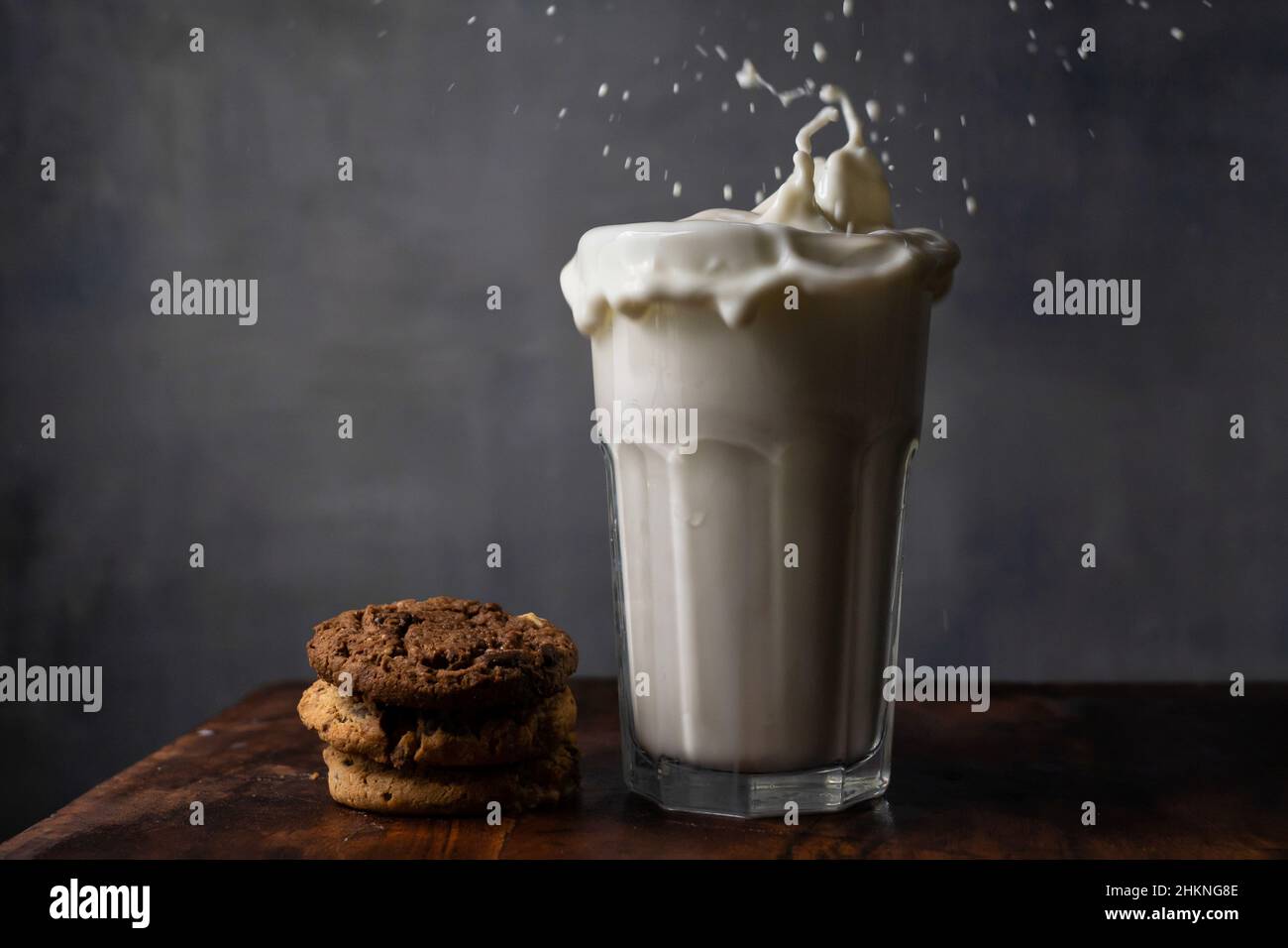 Milch in einem Glas spritzen und Schokoladenkekse auf einem Holztisch Stockfoto