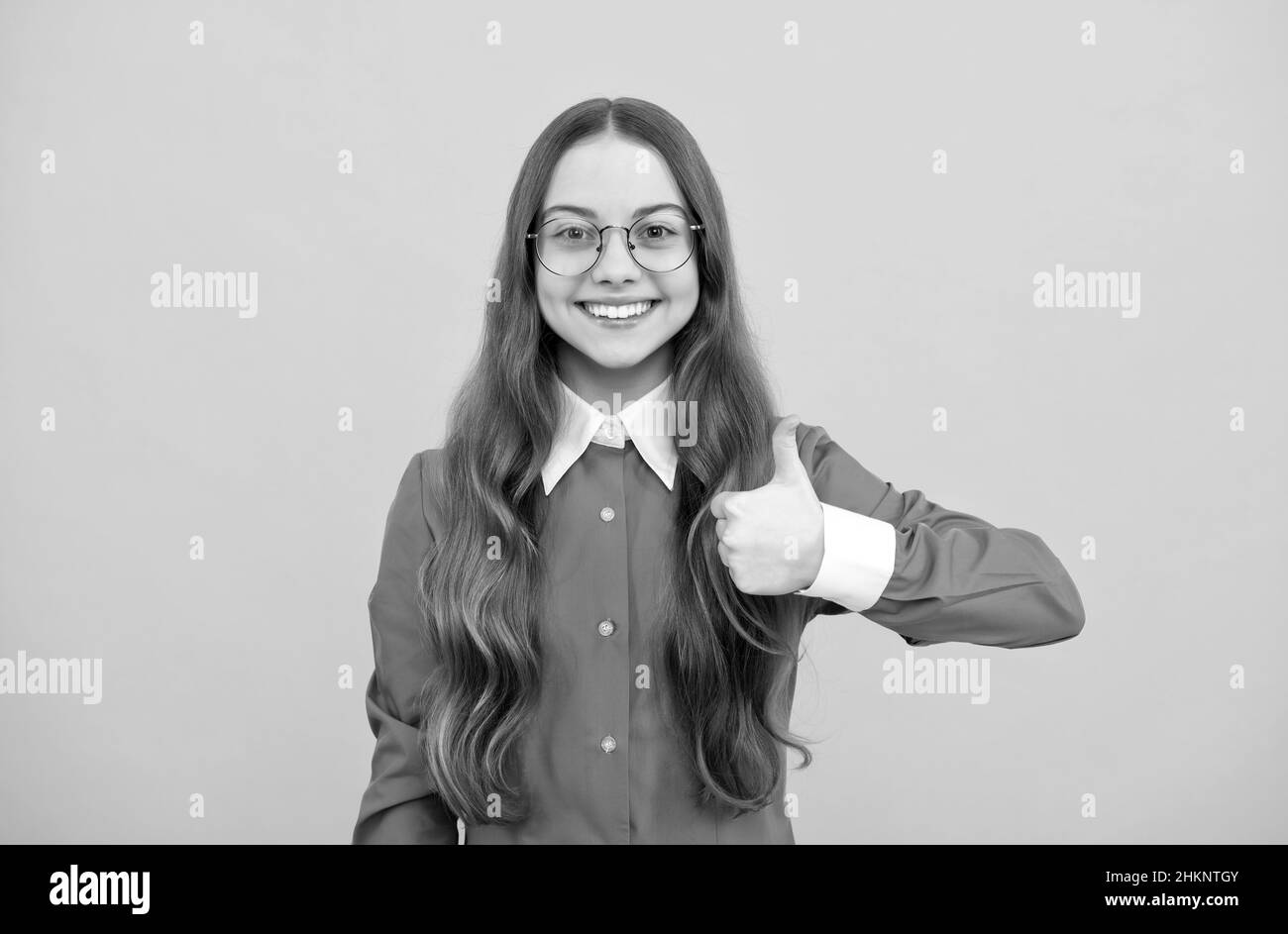 Glücklich nerdy aussehende Mädchen Kind geben Daumen nach oben Zufriedenheit Hand Geste gelben Hintergrund, Kindheit Stockfoto