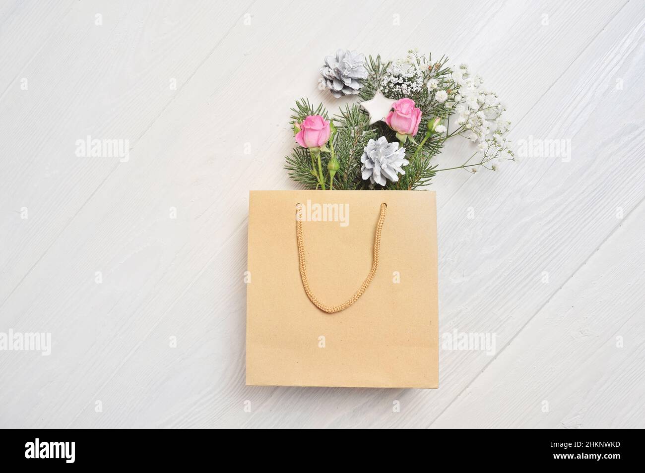 Weihnachts-Geschenkpaket mit Blumen und Zapfen auf weißem Holzhintergrund von oben. Einkaufs- und Rabattkonzept. Weihnachtsurlaub im Winter Stockfoto