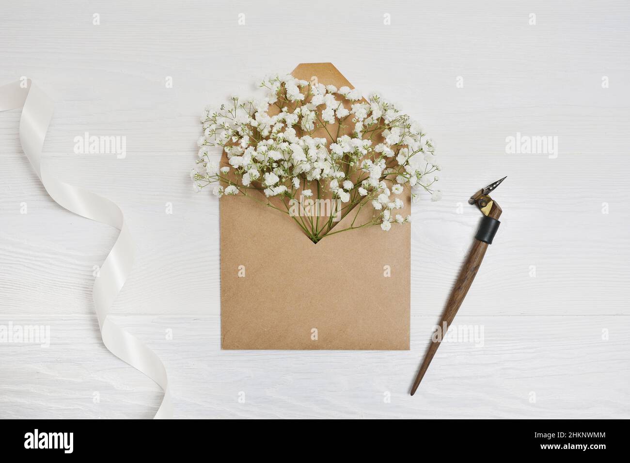 Kalligrafische Feder und Frühlingsumschlag mit Blumen und weißem Band, Grußkarte für Valentinstag mit Platz für Ihren Text. Flach liegend, Draufsicht Stockfoto
