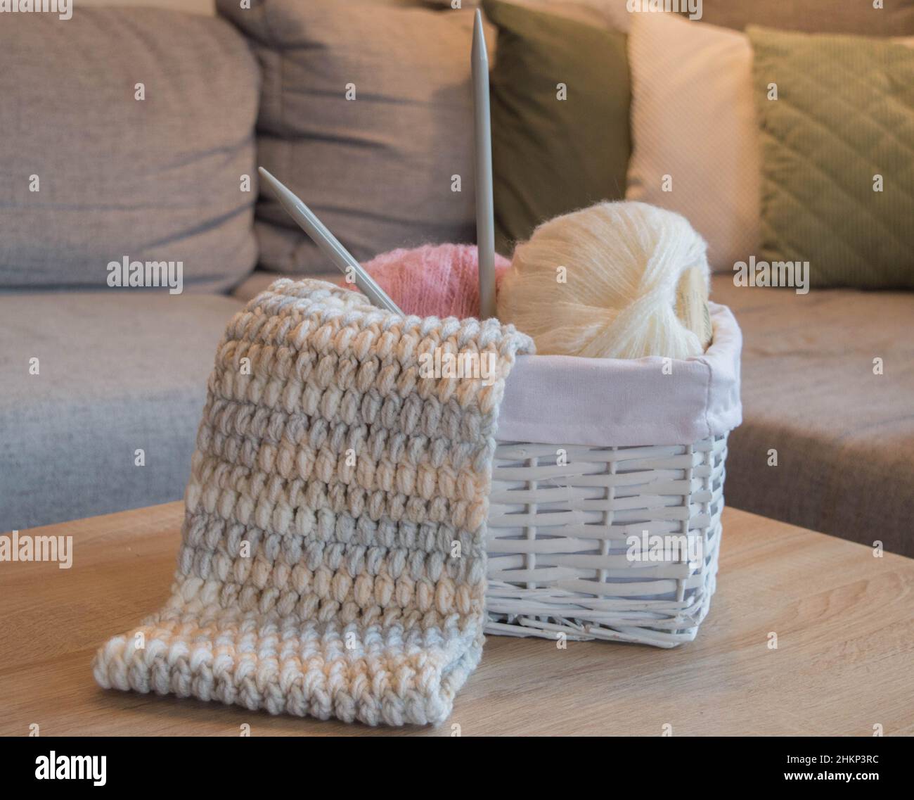 Rosa und weiße Wollkugeln in einem weißen Korb mit Stricknadeln und einem handgefertigten Strickschal Stockfoto