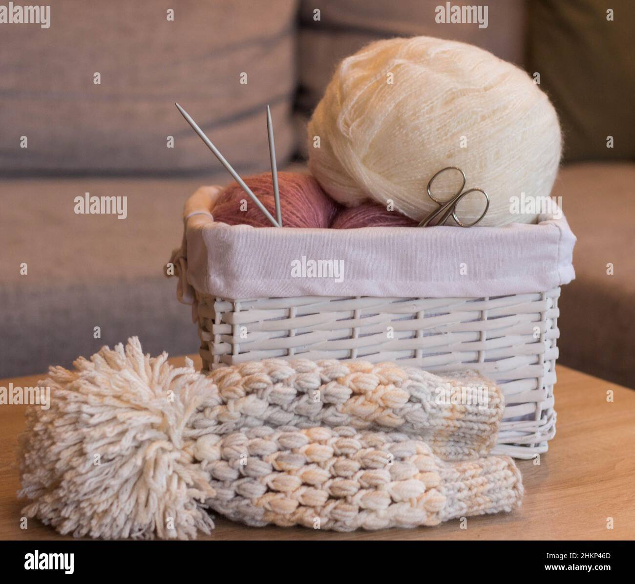 Rosa und weiße Wollkugeln in einem weißen Korb mit Stricknadeln und einem handgefertigten Strickhut Stockfoto