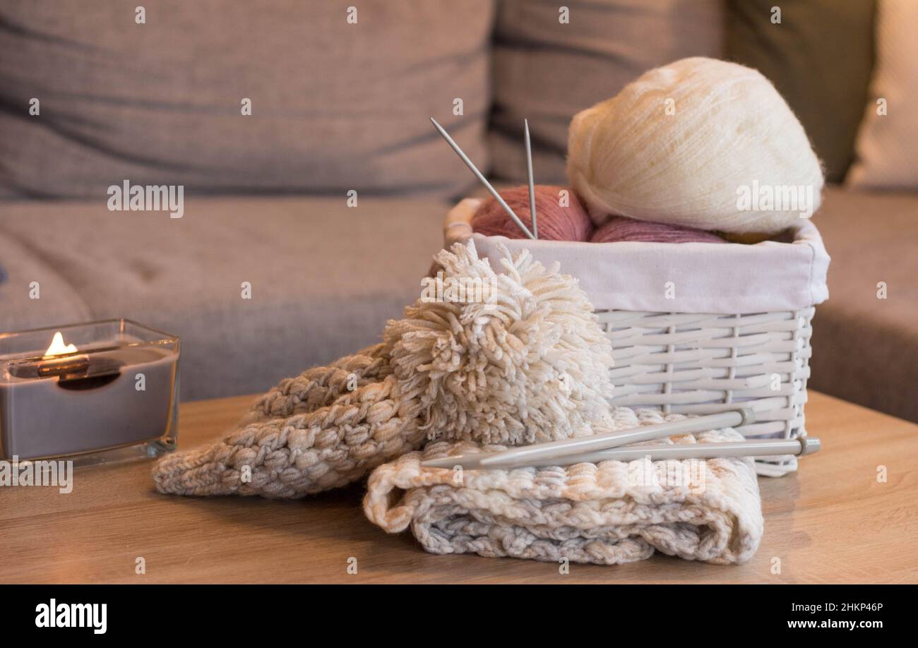 Rosa und weiße Wollkugeln in einem weißen Korb mit Stricknadeln und einem handgefertigten Strickhut Stockfoto