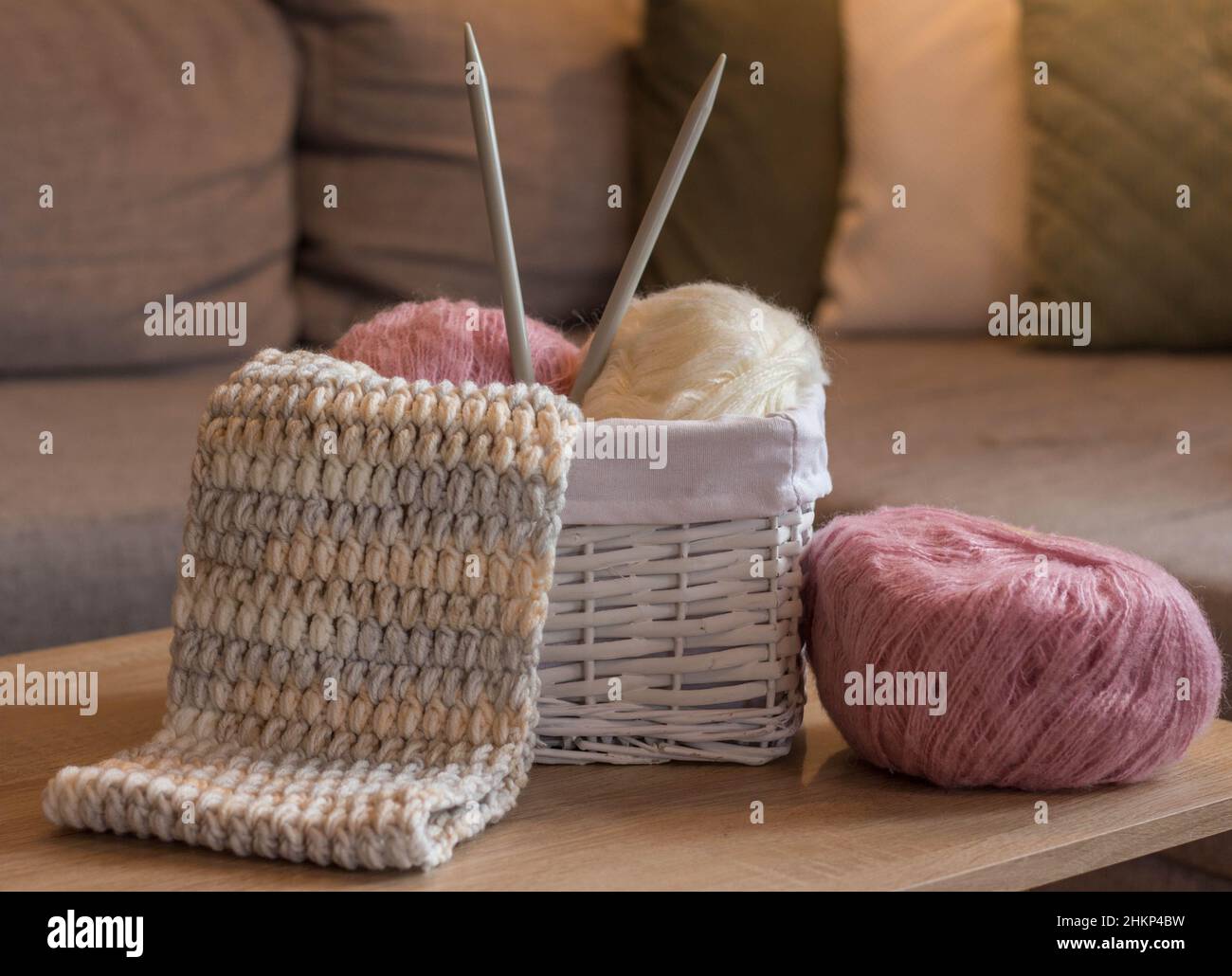 Rosa und weiße Wollkugeln in einem weißen Korb mit Stricknadeln und einem handgefertigten Strickschal Stockfoto