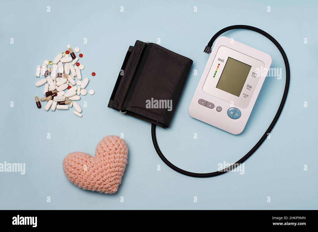 Ein Gerät zur Druckmessung, Tonometer auf blauem medizinischem Hintergrund, gestricktes Herz und Pillen. Kopfschmerzen, Behandlung von Bluthochdruck und Hypotonie. Stockfoto