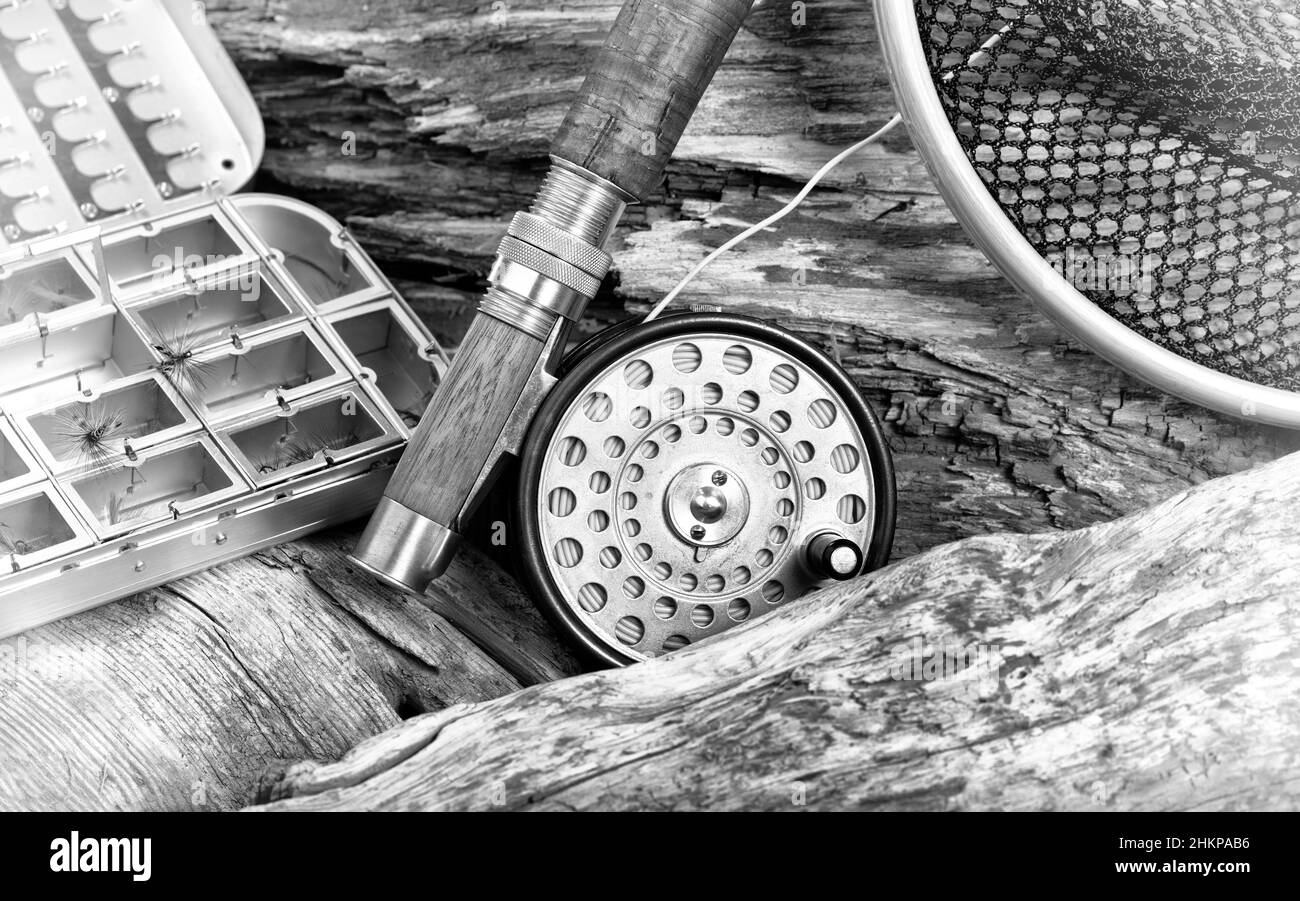 Antike Fliegenrute, Haspel, Landungsnetz und Köder Container in Stein und Drift Holz Flussbett Hintergrund mit Vintage-Effekt. Stockfoto