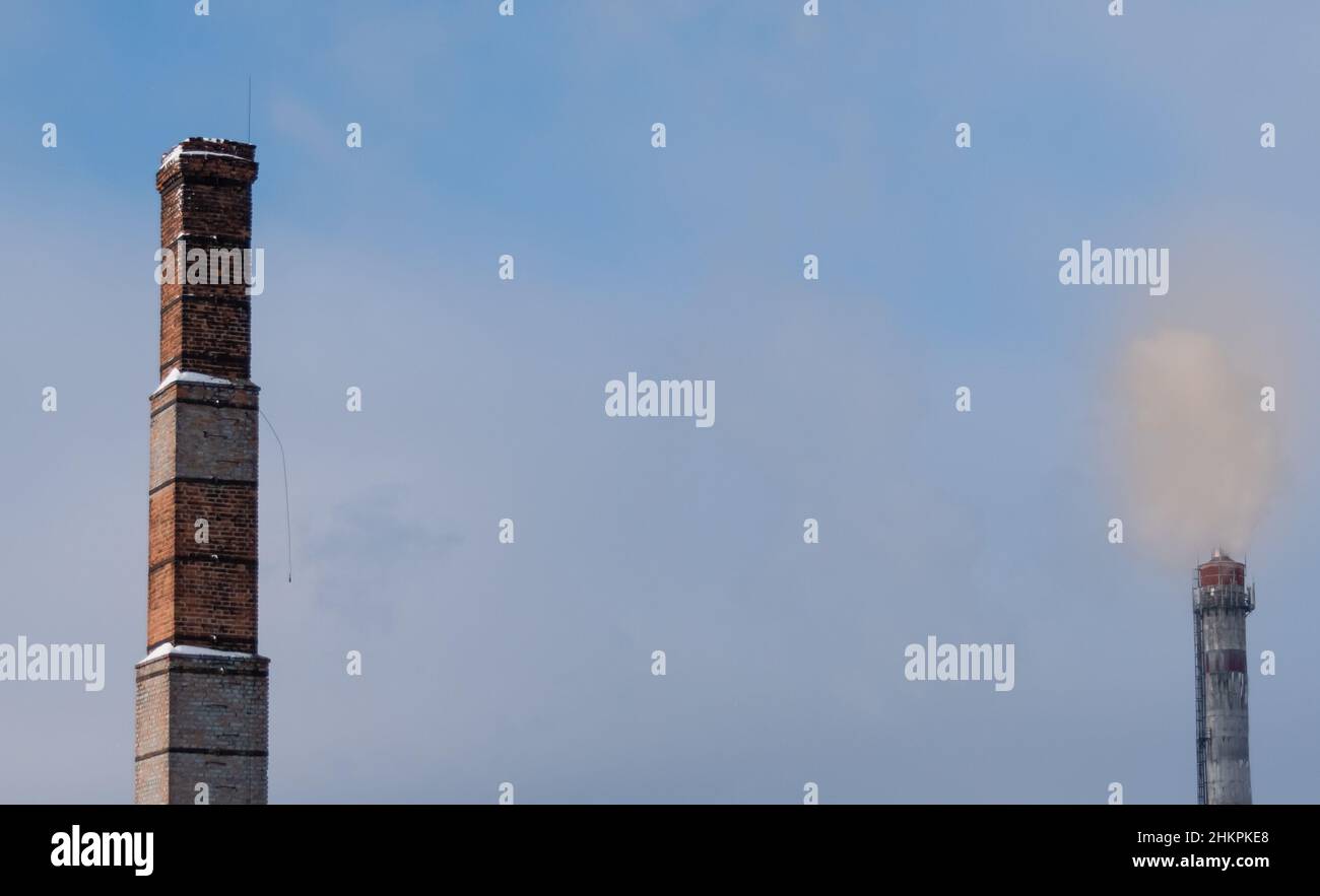 Alter Ziegelkamin auf verschwommenem Hintergrund von rauchigem Himmel und moderner Dampfleitung Stockfoto