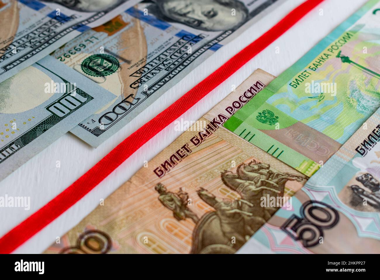 Rotes Band, das Banknoten von US-Dollar und russischen Rubel trennt. Fokus in der Bildmitte Stockfoto