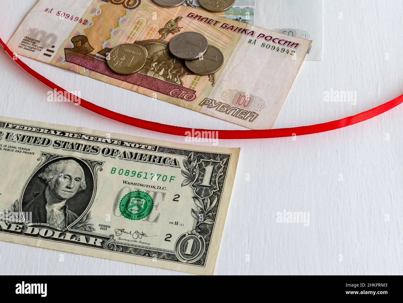 Rotes Band, das Banknoten einer US-Dollar-Banknote und russische Rubel mit Münzen auf weißem Hintergrund trennt Stockfoto