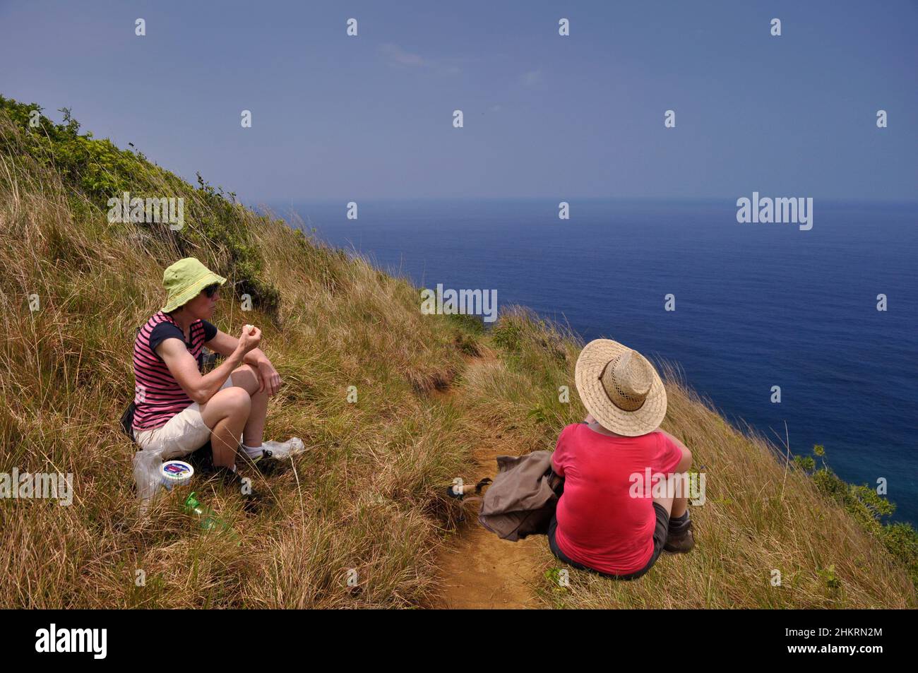 Zwei Frauen essen während einer Wanderung am Meer, Maui, Hawaii, USA. Die Pause, die nährt und erfrischt, mit Blick auf das Meer, auf einem Hügel. Stockfoto