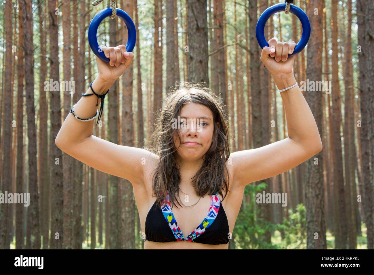 Porträt eines hübschen Teenagers, das vor dem Hintergrund eines Waldes auf Turnringen in der Natur aufzieht, Outdoor-Kurse Stockfoto