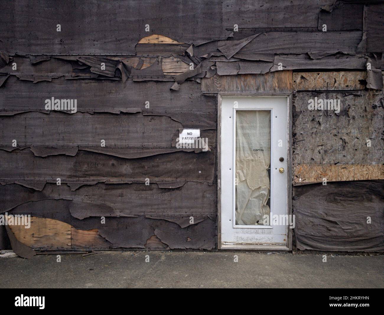 Verwittertes und abblätterndes Teerpapier oder Baupapier schält sich von der Außenwand eines alten, verlassenen Gebäudes in einer ländlichen Gemeinde weg. Stockfoto