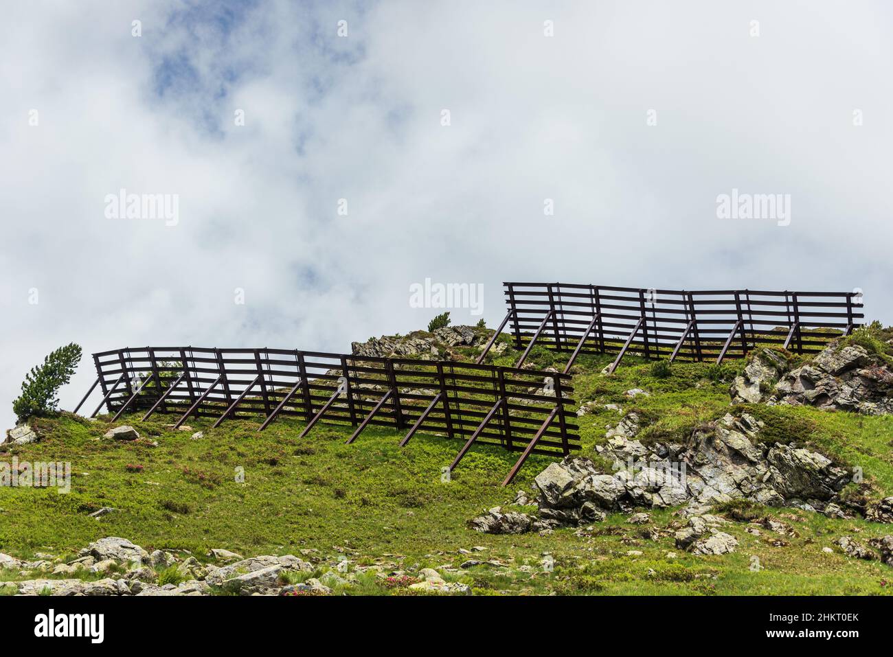 Lawinenschutzzäune in den alpinen Bergen. Stahlschneebrücken und gleitende Schneeständer. Sommer Berglandschaft. Stockfoto