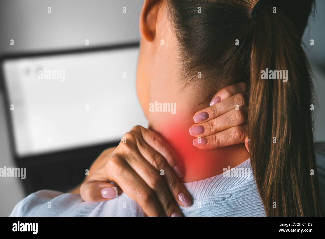 Nackenschmerzen nach der Arbeit am Computer. Junge Frau massiert Hals, um Schmerzen nach der Arbeit am pc zu lindern Stockfoto