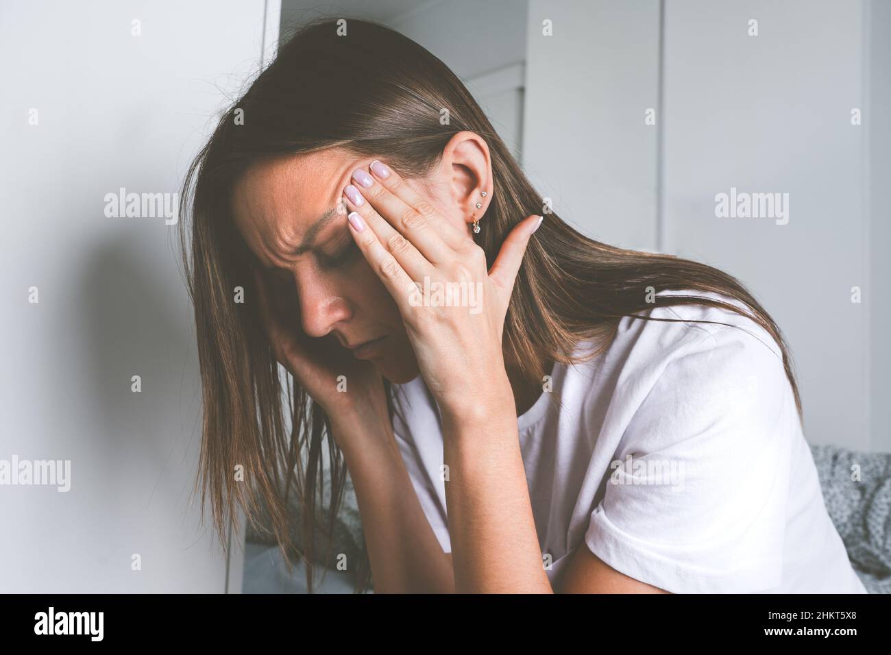 Junge Frau, die ihre Schläfe berührt und nach dem Aufwachen an Kopfschmerzen, Kopfschmerzen oder Migräne leidet Stockfoto