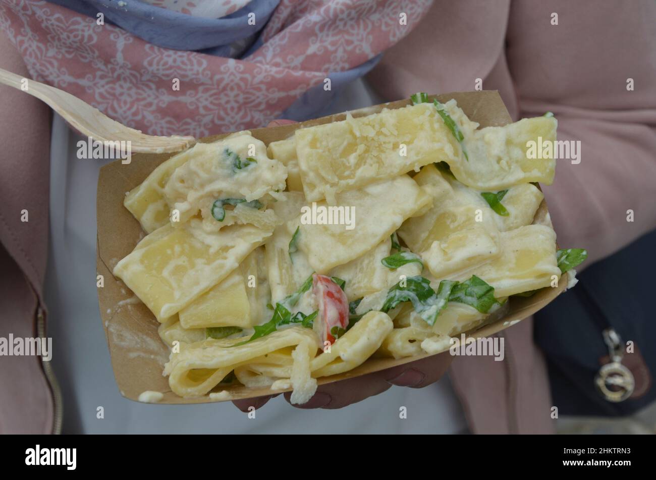 Die junge Frau isst Tagliatelle mit Käsesoße in einer Pappschale Stockfoto