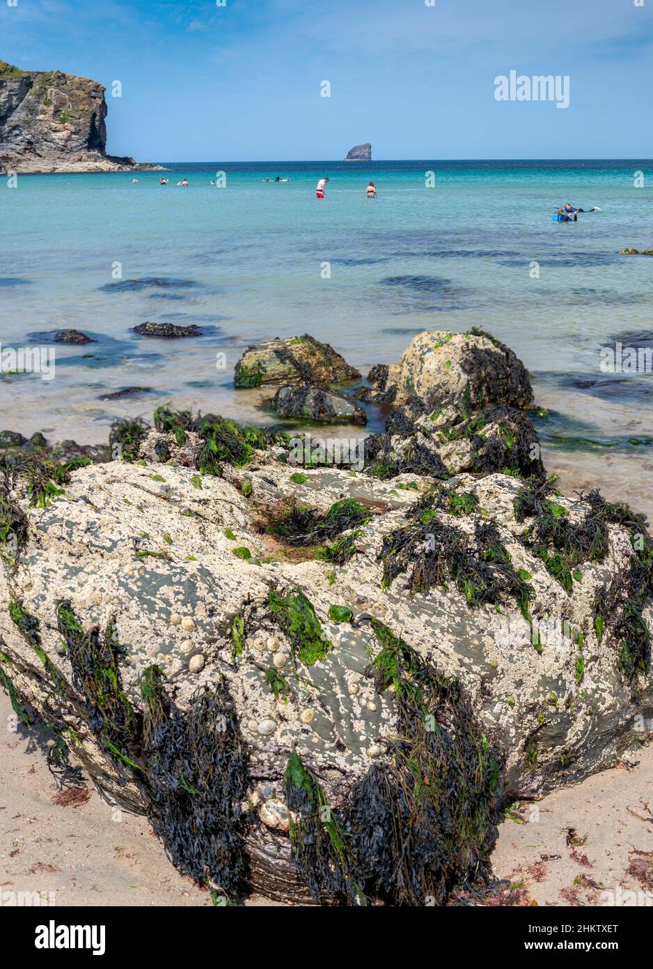 St.Agnes,Cornwall,England,UK-Juli 22: Urlauber genießen das warme Wasser des Atlantischen Ozeans,an einem sonnigen, heißen Mittsommertag, einen großen Felsbrocken Stand n Stockfoto