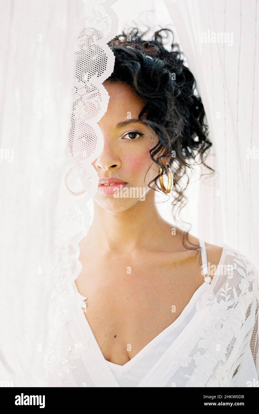 Porträt einer Frau in einem weißen Kleid, die hinter einem Vorhang aus guckt Stockfoto