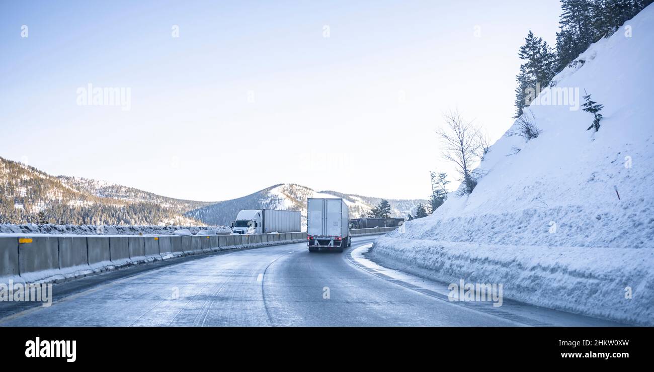 Industrielle Großgeräte Semi-Trucks mit Sattelaufliegern, die mit Fracht aufeinander zu laufen auf der kurvenreichen gefährlichen, rutschigen Winterautobahn mit Sno Stockfoto