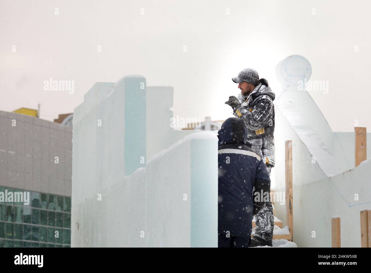 Ein Arbeiter in einer Winterjacke mit Kapuze und einer Strickmütze aus Wolle mit Visier am Arbeitsplatz Stockfoto