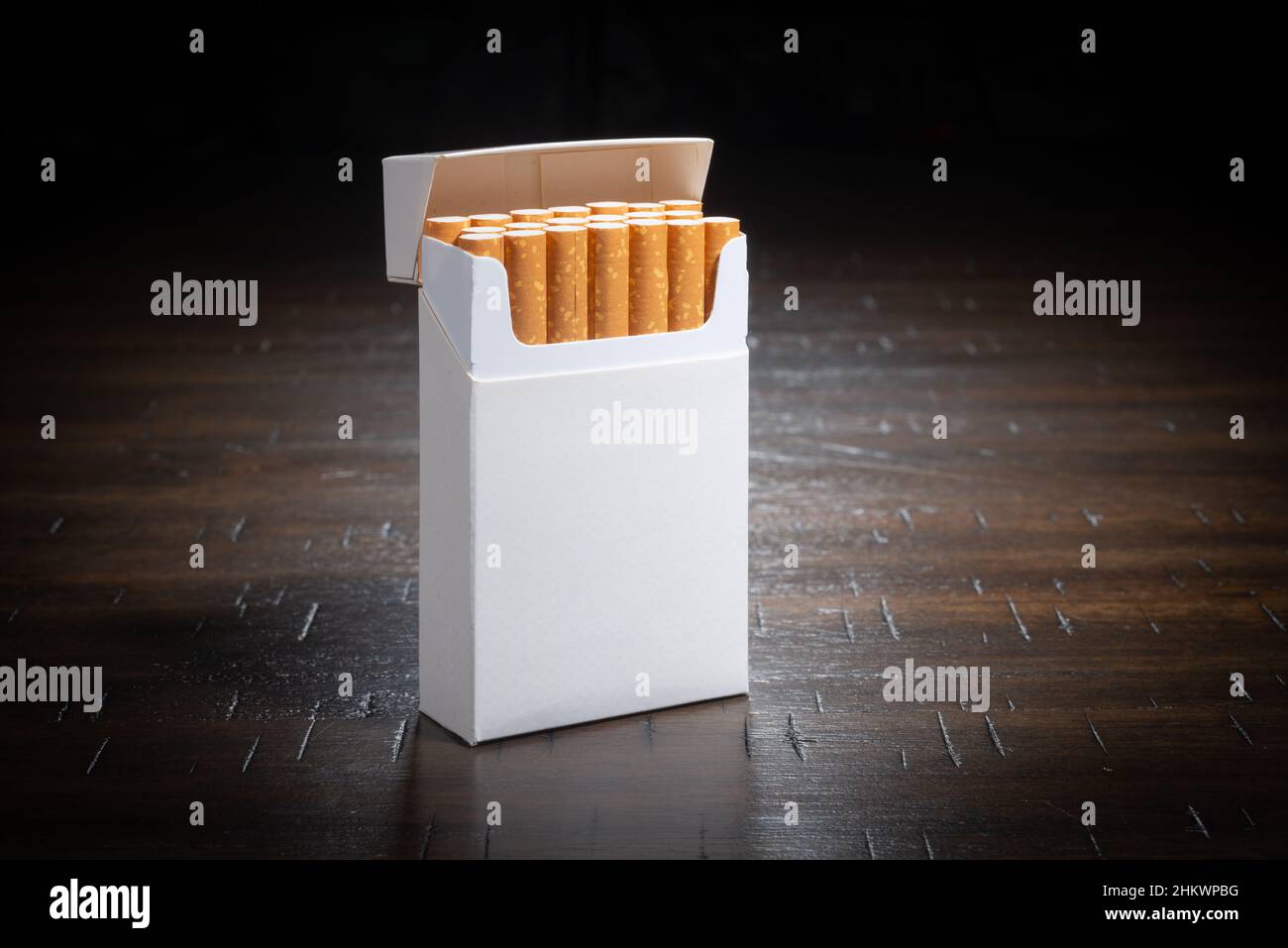 Auf einem Holztisch sitzt eine gewöhnliche, nicht gebrandete Zigarettenschachtel. Stockfoto