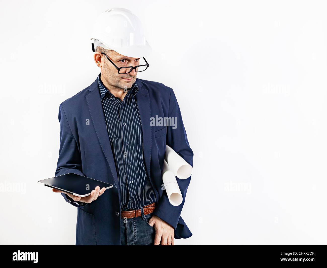 Ein Ingenieur in einem weißen, harten Helm hält einen Tablet-Computer und Blaupausen. Ein Mann mittleren Alters in einer blauen Jacke. Isoliertes Porträt auf weißem Hintergrund Stockfoto