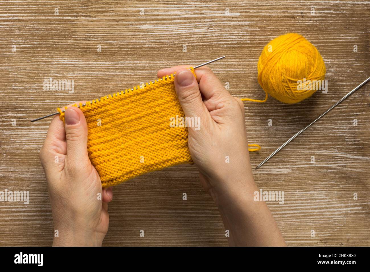 Frau Hand hält Strickmuster falsche Seite durch gelbe Garn auf dem Holzhintergrund Stockfoto