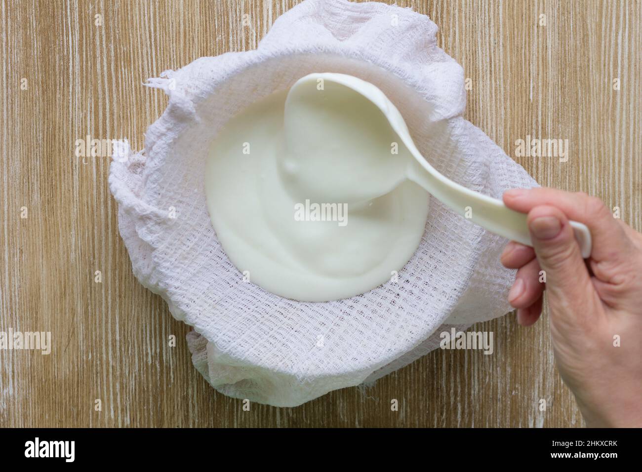 Die griechische Joghurtfrau machte es mit einem Kochlöffel auf einem Waffeltuch, um es auf dem Holzhintergrund dick zu machen Stockfoto