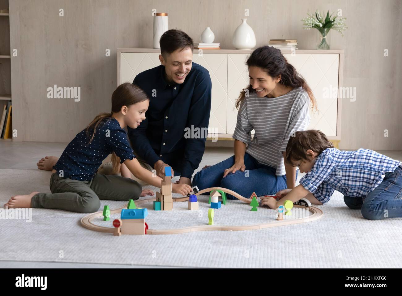 Glückliche Eltern und zwei Kinder, die mit der Holzeisenbahn spielen Stockfoto